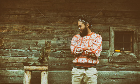 木屋前留着胡子猫的轻时髦男人的肖像图片