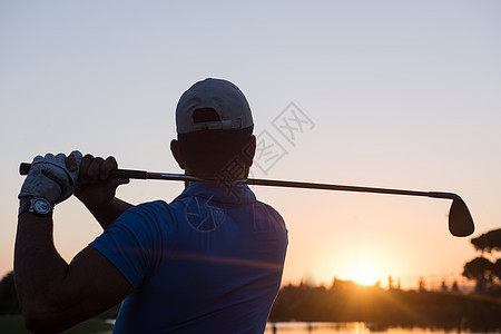 高尔夫球手美丽的日落时与司机球场上打远射图片