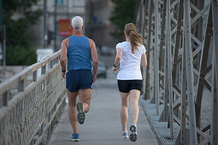 健康成熟的夫妇清晨城市慢跑,背景为日出图片