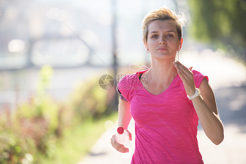 运动的女人清晨人行道上跑步,背景城市日出的场景图片