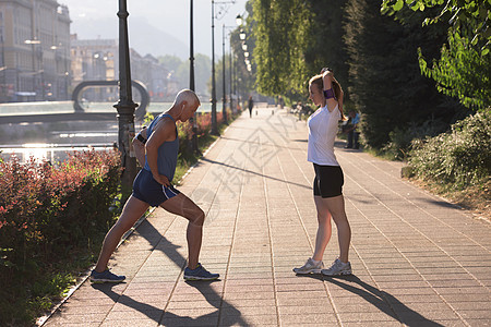 慢跑夫妇热身伸展之前,晨跑训练锻炼城市与日出背景图片