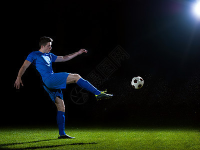 足球运动员足球场上踢球,黑色背景上被隔离图片