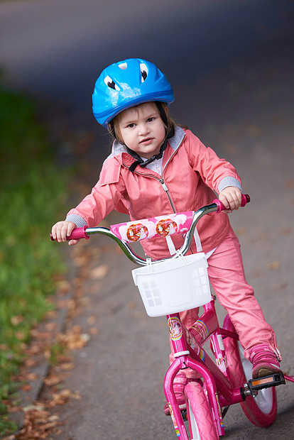可爱的微笑小女孩,骑着自行车头盔公园的路上图片