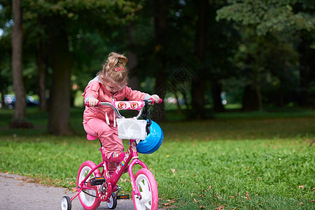 可爱的微笑小女孩,骑着自行车头盔公园的路上图片