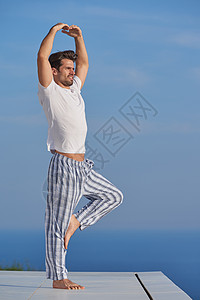 英俊的轻人现代家庭泰勒斯练瑜伽,背景海洋日落图片
