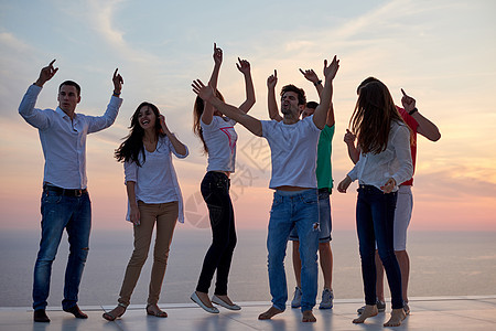 群快乐的轻人现代家庭的聚会上跳舞,玩得很开心,背景日落海洋图片