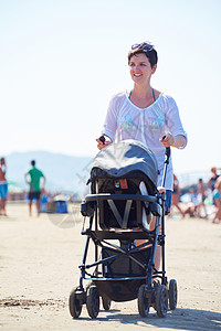 快乐的轻母亲海滩上散步,推着婴儿车图片