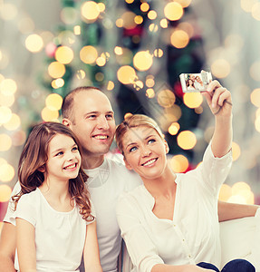 家庭,假期,技术人微笑的母亲,父亲小女孩用相机诞树灯光背景下自拍图片