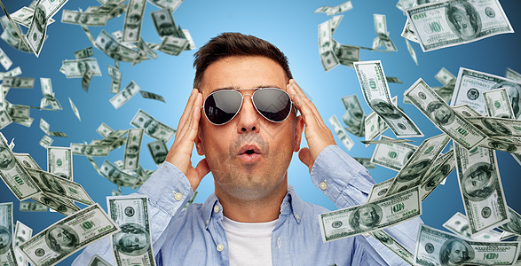 商业,金融,运气,财富人的害怕惊讶的中拉丁男子戴着蓝色背景的太阳镜,身上大量的美元贬值背景图片