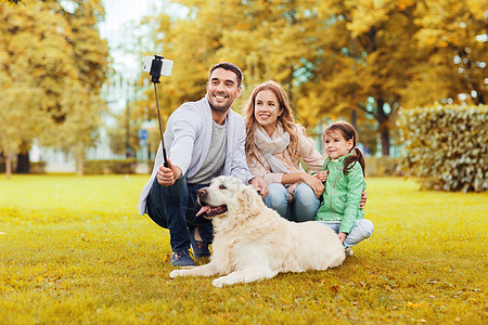 家庭,宠物,季节,技术人的快乐的家庭与拉布拉多猎犬狗秋天公园的自拍杆上用智能手机拍照图片