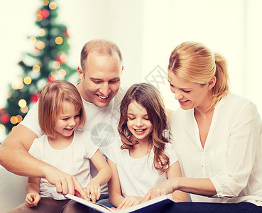 爱读书的孩子家庭,童,假期人微笑的母亲,父亲小女孩客厅诞树背景上看书背景