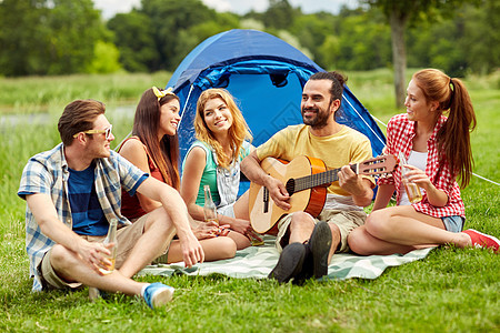 野餐人们的朋友带着帐篷饮料,露营时弹吉他图片