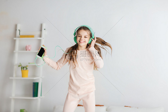 人们,孩子,睡衣派技术快乐的微笑女孩戴着耳机,用智能手机床上跳跃,家听音乐图片