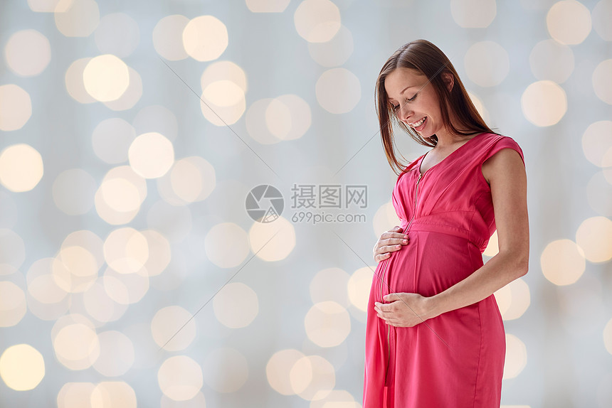 怀孕母亲人期望的快乐的孕妇大肚子假日灯光背景
