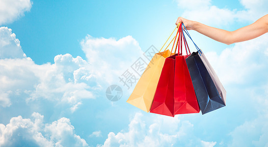 人,消费主义销售理念特写女手购物袋蓝天云彩的背景图片