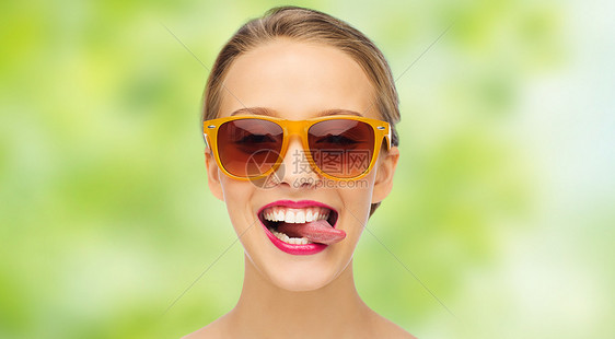 人,表情,快乐时尚的微笑的轻女人戴着太阳镜,嘴唇上涂着粉红色的口红,绿色的夏天背景上露出舌头图片