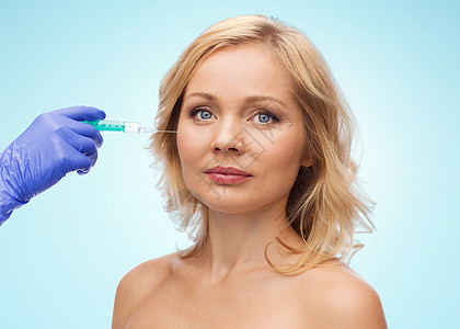 美容,抗衰容手术的中妇女的脸美容师携手手套注射器,蓝色背景下注射脸颊图片