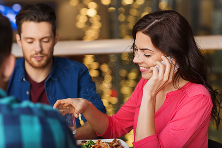 休闲技术生活方式人们的快乐的女人打电话给智能手机,朋友餐馆吃饭图片