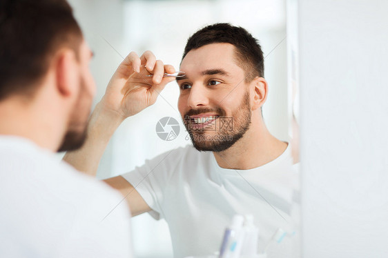 美丽人的微笑的轻人用镊子,镊子,眉毛家里的浴室浴室用镊子镊眉的男人图片