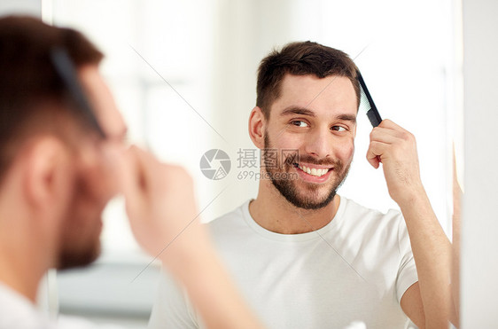 美丽,修饰人的微笑的轻人看着镜子,家里的浴室用梳子梳头图片