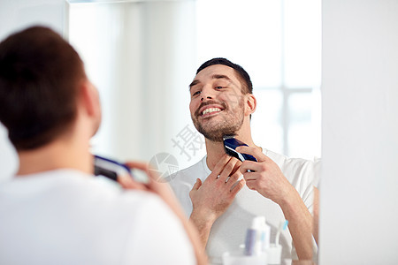 美容,卫生,剃须,美容人的轻人看着镜子剃须胡须与修剪机电动剃须刀家庭浴室图片