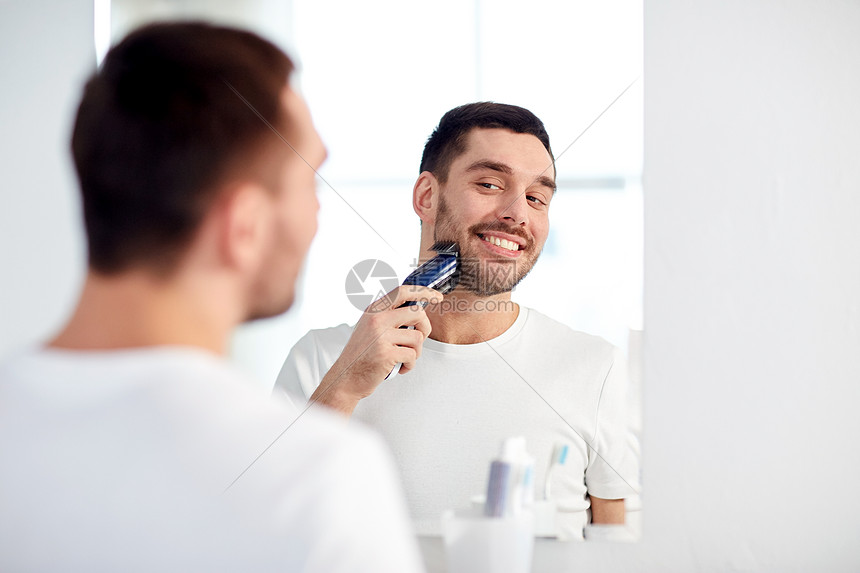 ‘~美容,卫生,剃须,美容人的轻人看着镜子剃须胡须与修剪机电动剃须刀家庭浴室  ~’ 的图片