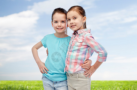 童,时尚,友谊人的快乐的微笑小女孩拥抱蓝天绿色的田野背景图片