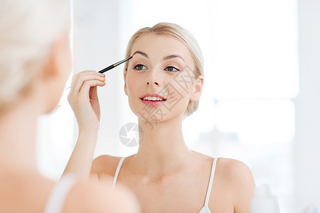 美容,化妆,化妆品,早晨人的轻的女人用刷子画眉,家里的浴室照镜子图片