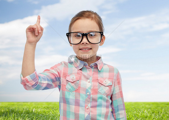 童,学校,教育,视觉人的快乐的小女孩戴着眼镜,手指指向蓝天绿色的田野背景图片
