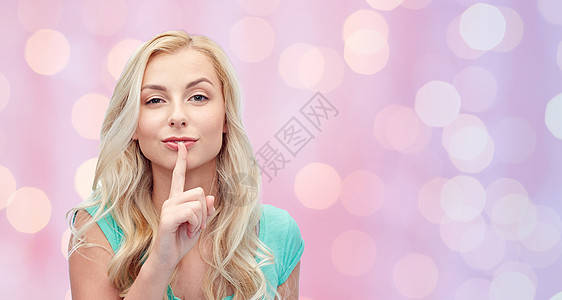 人,手势秘密美丽的轻女人握着手指她的嘴唇粉红色的节日灯光背景图片
