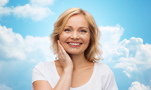 美丽,人护肤品的微笑的女人穿着白色衬衫,抚摸着蓝天云彩背景上的脸图片