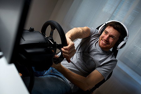 技术,游戏,娱乐活动人的快乐的微笑轻人耳机与个人电脑玩赛车电子游戏家里方向盘图片