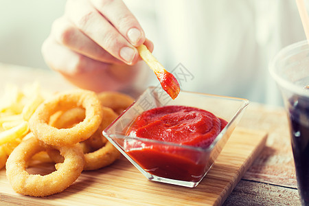 快餐,人健康的饮食观念用油炸鱿鱼圈,把炸薯条蘸木桌上的番茄酱碗里图片