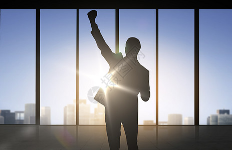 商业,成功,手势人的快乐商人举拳头庆祝胜利超过办公室窗口背景的剪影图片