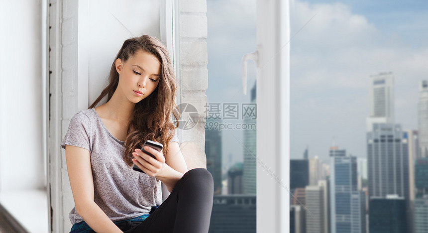 人,技术青少的悲伤快乐的漂亮少女坐窗台上与智能手机短信新加坡城市摩天大楼的背景图片