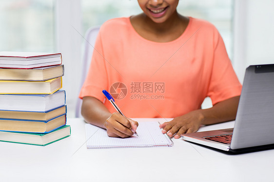 人,技术,学教育的接近快乐的非裔美国轻妇女坐桌子上,着笔记本电脑书籍,家里写字图片