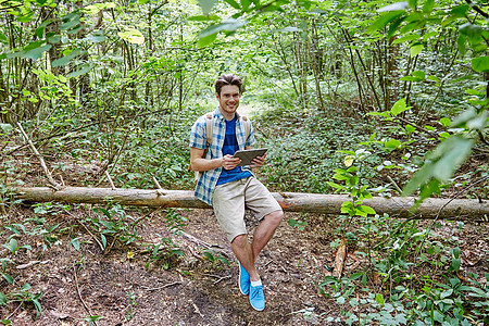 冒险,旅行,旅游,徒步旅行人们的快乐的轻人,背包平板电脑电脑坐树林里倒下的树干上图片