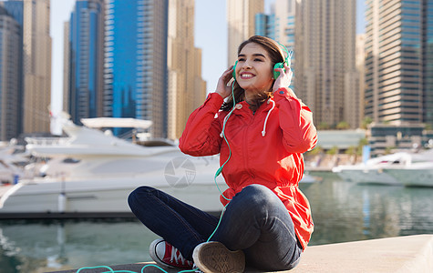 技术,旅游,旅游人的微笑的轻妇女十几岁的女孩戴着耳机,迪拜城市街道上听音乐,港口背景下听船只图片