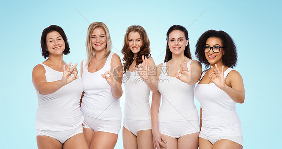 手势,友谊,美丽,身体积极人的群快乐的同的女人穿着白色内衣,蓝色背景上OK手牌图片