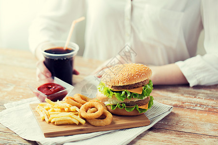 快餐,人健康的饮食靠近女人的手与汉堡包奶酪汉堡,炸薯条,鱿鱼圈可乐饮料坐桌子上图片