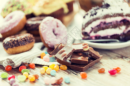 巧克力豆垃圾食品,糖果健康的饮食巧克力片,果冻豆,釉甜甜圈蛋糕木桌上背景