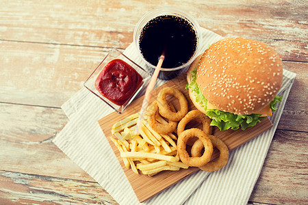 快餐健康的饮食汉堡芝士汉堡,油炸鱿鱼圈,炸薯条,可乐饮料番茄酱木桌上图片