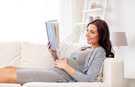怀孕母微笑的孕妇躺沙发上看书快乐的孕妇家看书图片