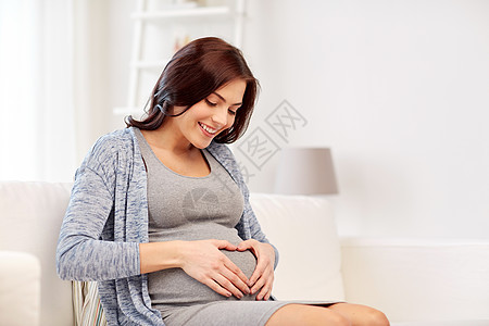 怀孕,爱,人期望的快乐的孕妇坐沙发上,家里手势图片
