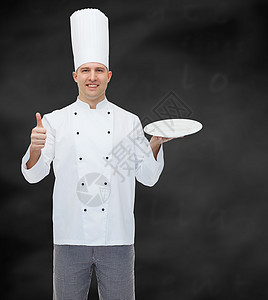 烹饪职业广告人的快乐的男厨师着空盘子里的东西,黑色的粉笔板背景上竖大拇指图片