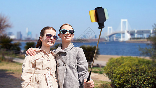 人,孩子,朋友技术快乐的女孩日本背景的东京彩虹桥上用智能手机拍照图片