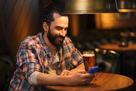 人与技术快乐的人与智能手机喝啤酒阅读信息酒吧酒吧智能手机啤酒的男人酒吧发短信图片