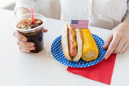 主义节日的妇女的手与热狗玉米持可口可乐饮料塑料杯图片