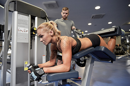运动,健身,队合作人的轻的妇女私人教练健身房的腿部卷曲机上弯曲肌肉图片