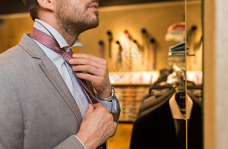 销售,购物,时尚,风格人的接近轻人穿着西装,选择捆绑领带,并商场服装店照镜子图片